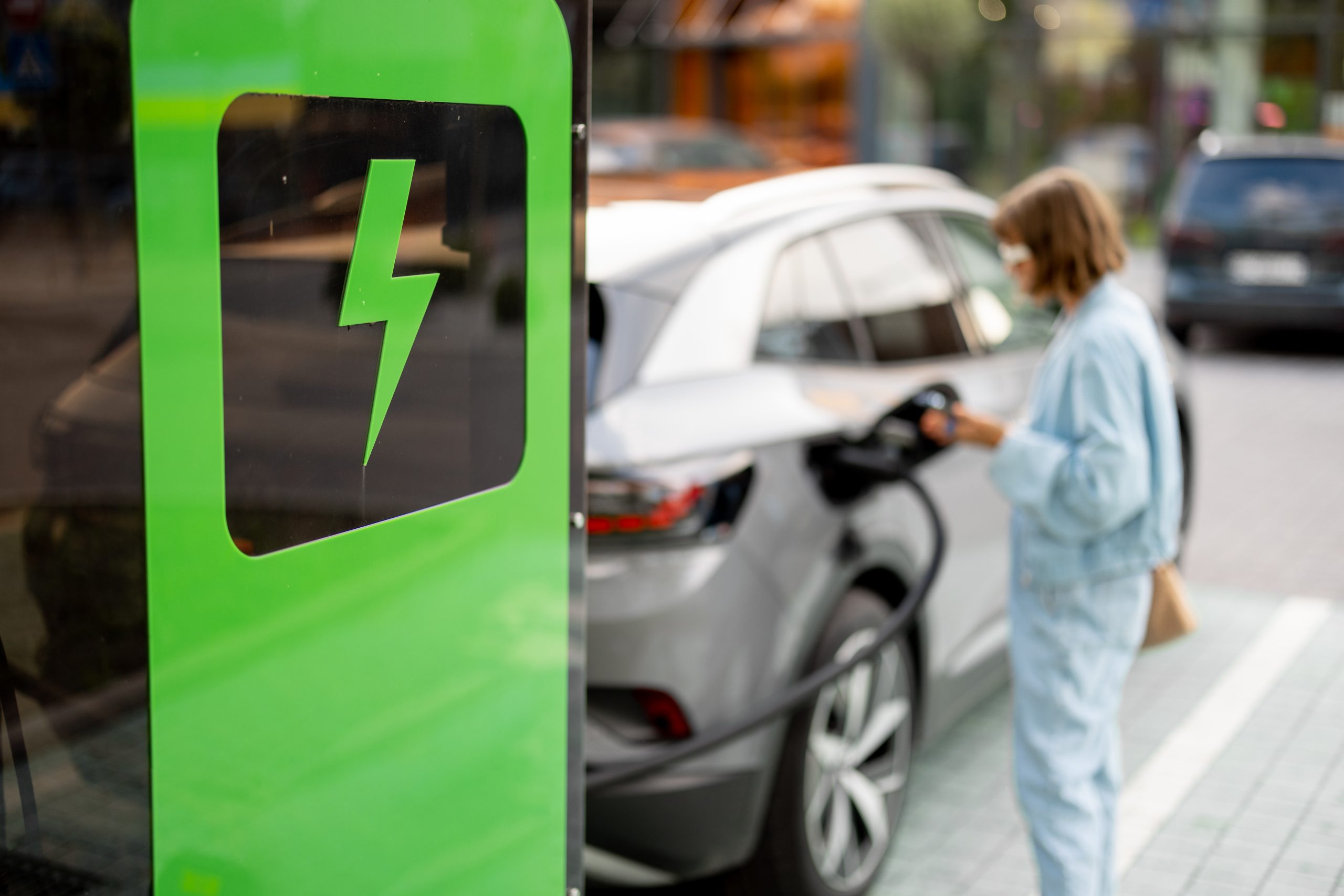 Young woman plugs in a cable for vehicle fast charging on a public charging station outdoors. Concept of electric car charging, electricity and green energy for driving